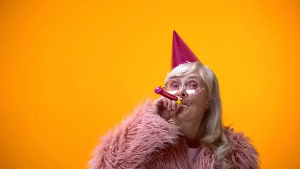 Photo of Glamorous aged woman blowing party horn, celebrating birthday anniversary