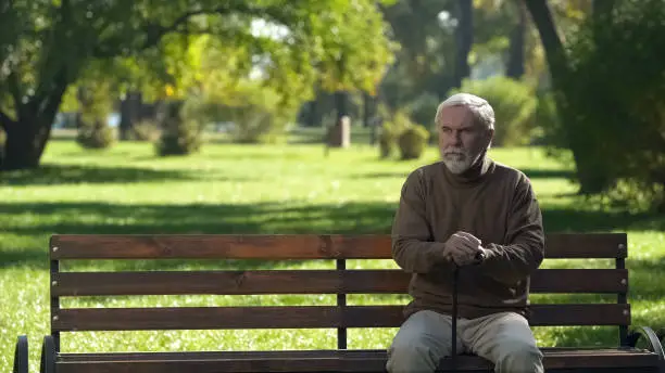 Old man with walking cane sitting on bench, resting after walking in park
