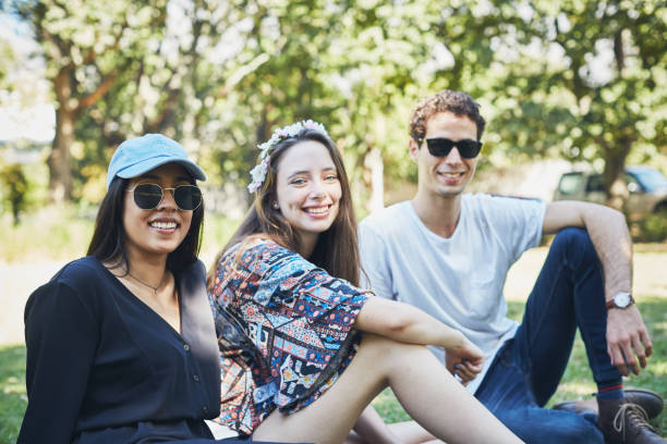 istock Three young people sitting in park smile 1143240355