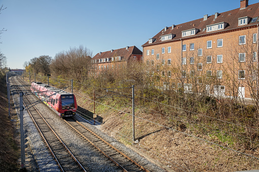 Valby, Copenhagen, Denmark - April 15, 2019: Typical house with flats close to the railroad tracks and a commuters train in a suburb outside Copenhagen