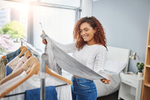 Shot of a young woman going through clothes from her wardrobe at home