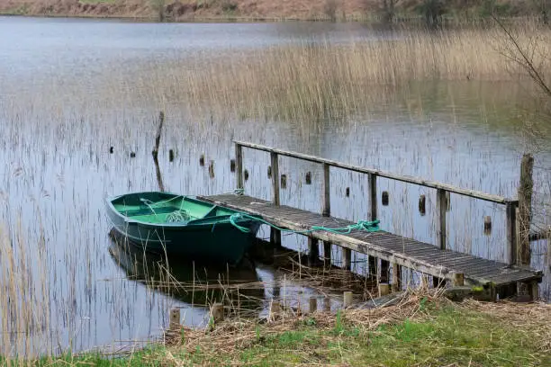 Green rowing boat tied with rope to wooden jetty pier in lake loch within Argyll Scotland uk