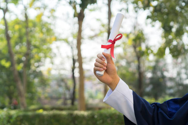 nahaufnahme junge mann mit graduiertenkleid und mit zertifikatspapier mit band nach abschluss der graduiertenkunde, leistungskonzept - bachelors degree stock-fotos und bilder