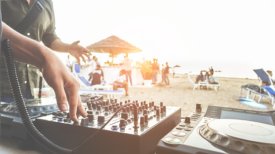 Dj mixing at sunset beach party in summer vacation outdoor - Disc jockey hands playing music for tourist people in chiringuito kiosk bar - Event, music and fun concept - Focus on right hand