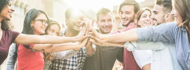 Photo of Young happy people stacking hands outdoor - Diverse culture students celebrating together - Youth lifestyle, university, relationship, human resorces, work and friendship concept - Focus on hands