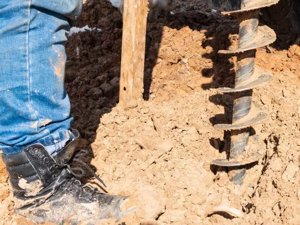 Photo of Man drills a geological well. Close up of boot, screw and soil