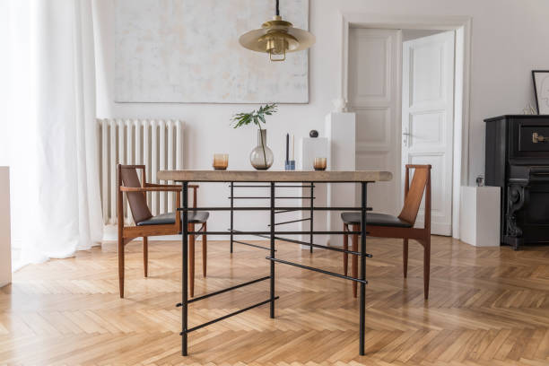 istock Eclectic and elegant dining room interior with design sharing table, chairs, gold pendant lamp, abstract paintings, piano and stylish accessories. Minimalistic decor. Brown wooden parquet. Real photo. 1143252279