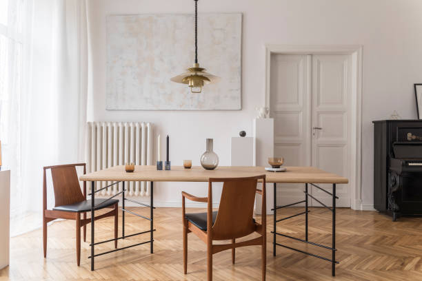istock Eclectic and elegant dining room interior with design sharing table, chairs, gold pendant lamp, abstract paintings, piano and stylish accessories. Minimalistic decor. Brown wooden parquet. Real photo. 1143252405