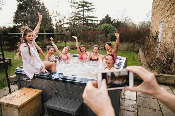 Smile for the Photo! Small group of female friends relaxing and celebrating in a hot tub. They are all looking towards their friend who is taking a group photo of them. hot tub stock pictures, royalty-free photos & images