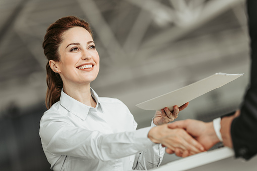 Low angle portrait of beaming girl greeting male hand while giving document him. Glad employer during job concept