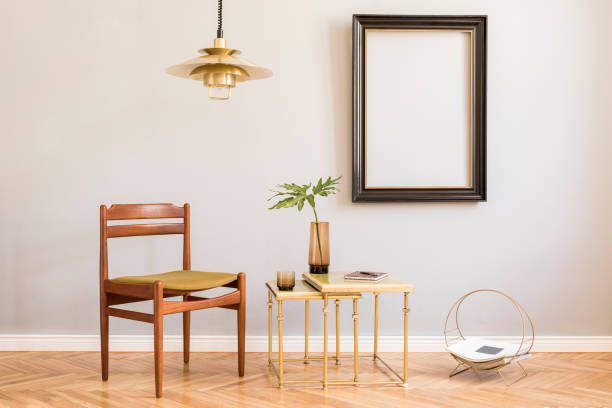 istock Design retro interior with design gold lamp, small tables with tropical leaf in vase and stylish accessories. Black mock up frame on the grey background wall. Minimalistic concept of sitting room. 1143253481