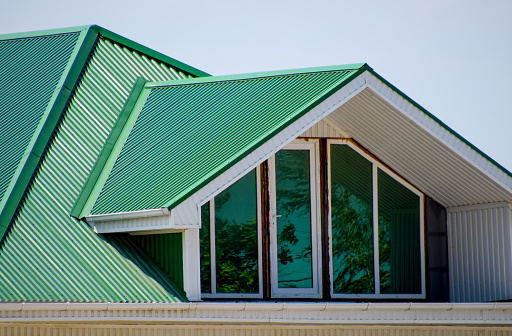 La casa con ventanas de plástico y un tejado verde de chapa corrugada. Techo verde de Perfil de metal ondulado y ventanas de plástico. photo