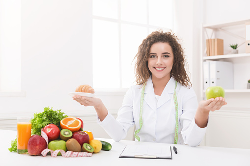 Fruit versus bakery products. Woman nutritionist holding apple and croissant in hands, preparing to choose your nutrition, copy space