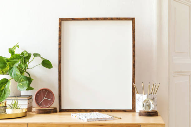 istock Modern scanidnavian interior with mock up photo frame, design office accessories and plants on the wooden desk. Beautiful mirror on the white wall. Creative desk of home decor. Warm and sunny room. 1143255690