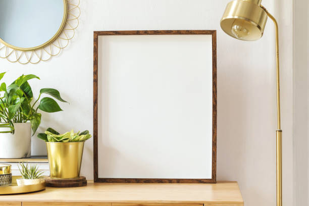 Modern scanidnavian interior with mock up photo frame, design office accessories and plants on the wooden desk. Beautiful mirror on the white wall. Creative desk of home decor. Warm and sunny room.