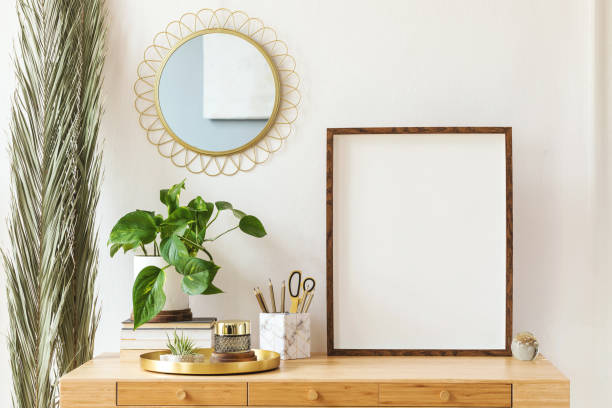 istock Modern scanidnavian interior with mock up photo frame, design office accessories and plants on the wooden desk. Beautiful mirror on the white wall. Creative desk of home decor. Warm and sunny room. 1143255928