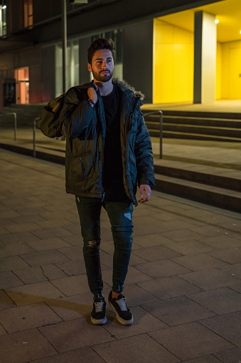 Young man carrying a gym bag at night in a city street in winter.