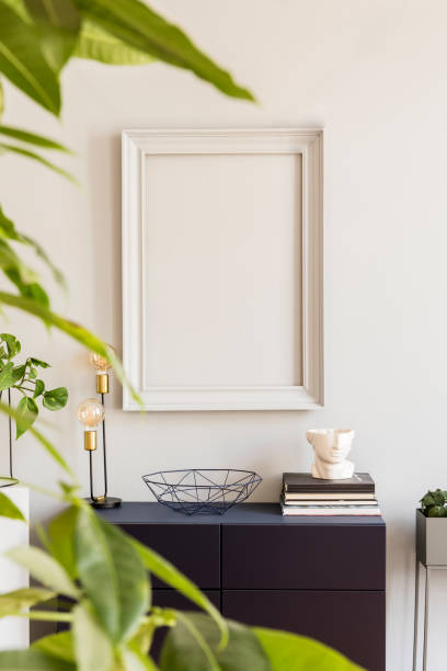istock Scandinavian and design home decor with mock up gray poster frame, navy blue shelf with stylish accessories, lamp and plants. Stylish and minimalistic room interior with big plant. Template. Blank. 1143256251
