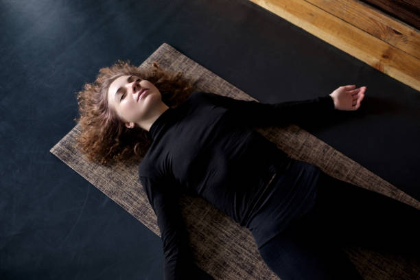 woman practicing in a yoga studio resting in shavasana or corps pose - corps imagens e fotografias de stock