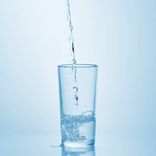 istock Pouring water into glass on white background. Water spilled on the table. 1143260251