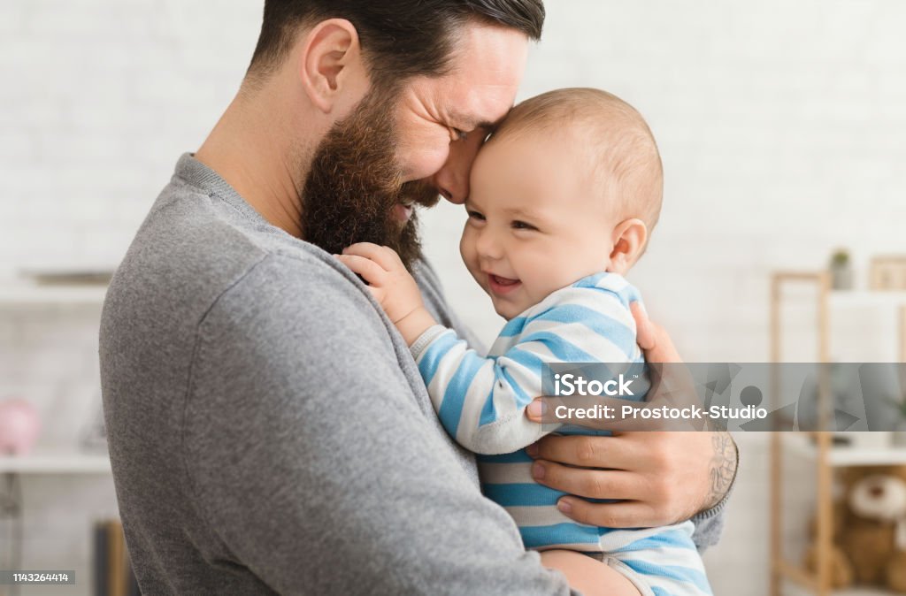 Loving father embracing his cute baby son Cheerful father and son cuddling at home, enjoying time together Father Stock Photo