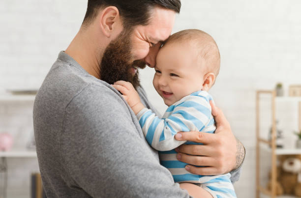 Loving father embracing his cute baby son Cheerful father and son cuddling at home, enjoying time together father and baby stock pictures, royalty-free photos & images