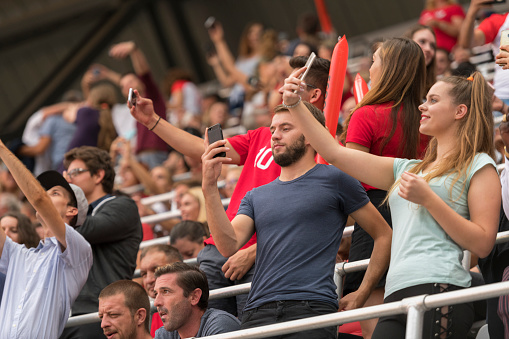 Football fans taking selfie with smart phone while watching match in stadium.