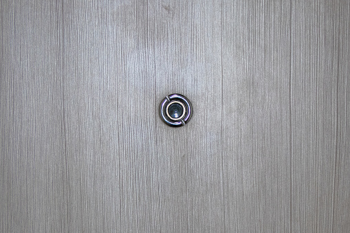 Close up door lens peephole on white wooden texture.