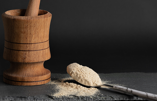 Pila de Maca en polvo y Pounder de madera en superficie de tabla de corte de piedra y fondo negro. Concepto de suplemento de Maca superfood. photo