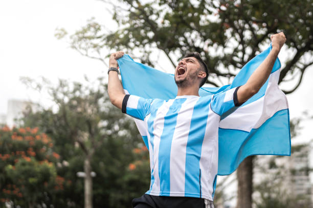 männlicher fan feiert und hält argentinische fahne - argentina stock-fotos und bilder