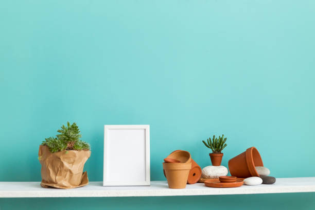 istock Modern room decoration with picture frame mockup. White shelf against pastel turquoise wall with pottery and succulent plant with potted succulent plant. 1143275251