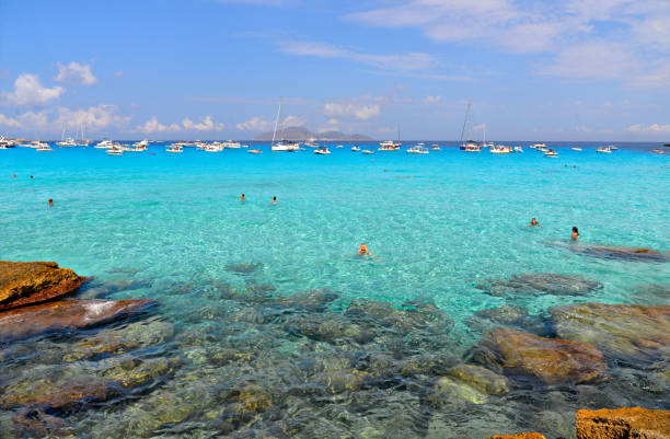 people inside paradise clear torquoise blue water with boats and cloudy blue sky in background in Favignana island, Cala Rossa Beach, Sicily South Italy. 02.09.2018. people inside paradise clear torquoise blue water with boats and cloudy blue sky in background in Favignana island, Cala Rossa Beach, Sicily South Italy. egadi islands photos stock pictures, royalty-free photos & images