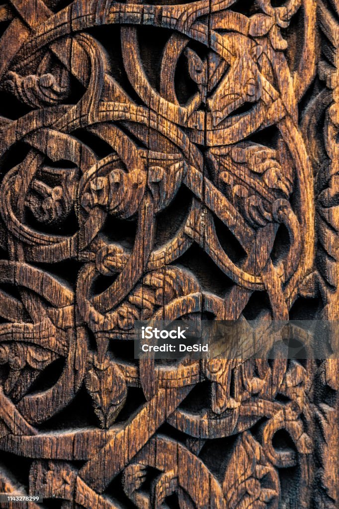 Detailed pattern of ancient vikings in Norway Ornaments of ancient vikings on a wooden surface. External wooden wall carved decoration of medieval Stave church with viking motifs covered with tar. Detailed pattern of ancient vikings in Norway. Viking Ship Stock Photo
