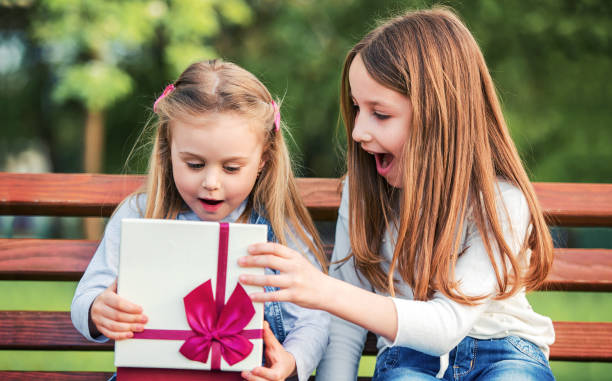 Present for a younger sister. Family concept Cute little girl surprised her younger sister with a birthday present. Family concept happy birthday cousin images stock pictures, royalty-free photos & images
