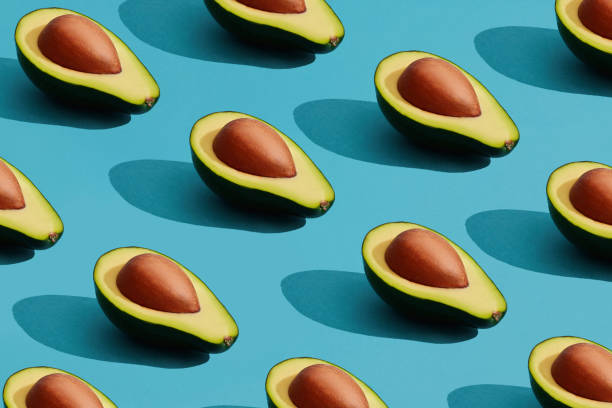 istock Colorful fruit pattern of fresh cutted avocado halves with pits on blue pastel background 1143279929