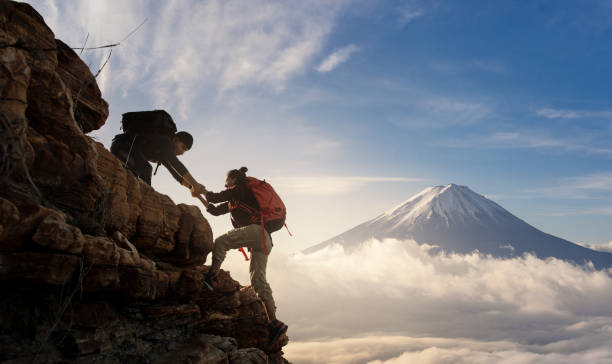 アジアハイキングのグループは、太陽の光で山のシルエットをお互いに助けます。 - people traveling journey group of people hiking ストックフォトと画像