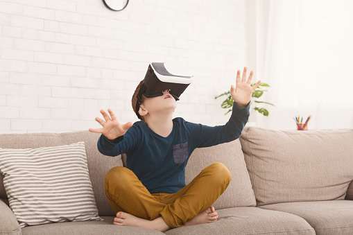 Modern technology. Boy in virtual reality headset playing videogame at home