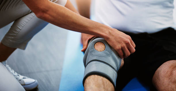 Taking careful measures until he get's back to full fitness Shot of an unrecognizable female physiotherapist strapping a knee brace on a male patient knee brace stock pictures, royalty-free photos & images