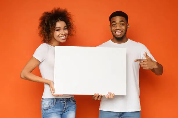 Photo of Young happy couple holding blank white board