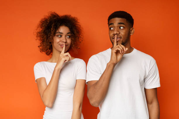 Amazed black couple make silence sign, keep forefingers on lips