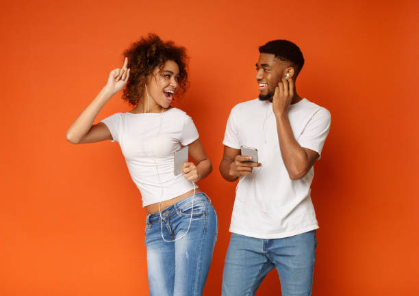 homme et femme noirs dans des écouteurs écoutant la musique sur des téléphones cellulaires - female likeness audio photos et images de collection