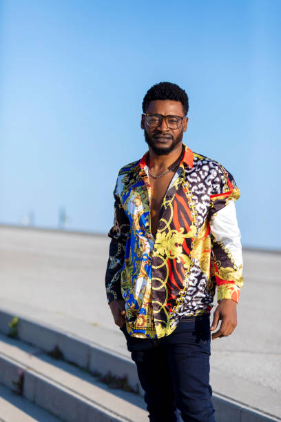 istock Front view of young black man wearing eyeglasses standing against blue sky while looking camera 1143287612