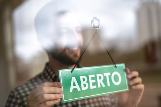 geschäftsinhaber drehen sich als offen (aberto auf portugiesisch) für geschäftszeichen in der schaufensterscheibe - geschäftseröffnung stock-fotos und bilder