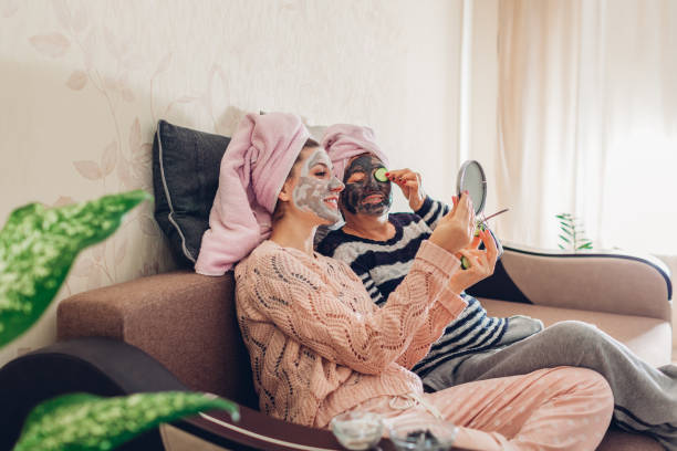 mother and her adult daughter applying facial masks and cucumbers on eyes. women chilling and having fun at home - facial mask spa treatment cucumber human face imagens e fotografias de stock