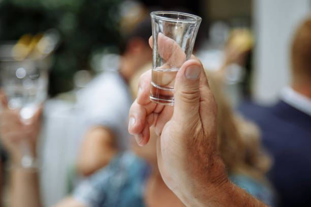 mão do homem que prende um vidro com vodca. - copo pequeno para bebida alcoólica - fotografias e filmes do acervo