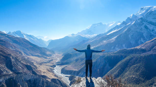 Nepal - Man spreads her hands wide, Manang Valley Man wearing a beanie and blue jumper, spreads his arms wide, breathing deeply the fresh mountain air. His gesture represents freedom and happiness. Below a long valley stretches in Himalayas. annapurna circuit photos stock pictures, royalty-free photos & images