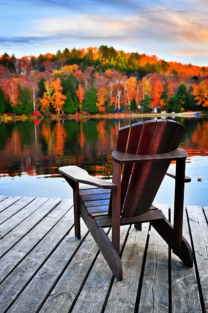 Photo of A wooden chair on a wooden deck beside an autumn lake