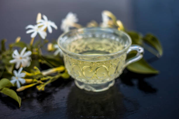 Close up of tea of Indian jasmine flower or juhi or Jasminum Auriculatum on wooden surface  in a glass cup with raw flowers. Close up of tea of Indian jasmine flower or juhi or Jasminum Auriculatum on wooden surface  in a glass cup with raw flowers. jasminum auriculatum flowers stock pictures, royalty-free photos & images