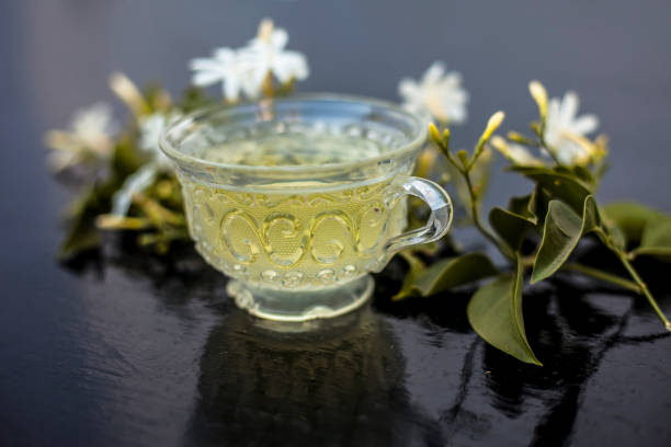 Close up of tea of Indian jasmine flower or juhi or Jasminum Auriculatum on wooden surface  in a glass cup with raw flowers. Close up of tea of Indian jasmine flower or juhi or Jasminum Auriculatum on wooden surface  in a glass cup with raw flowers. jasminum auriculatum flowers stock pictures, royalty-free photos & images