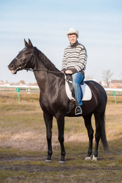istock Man riding horse, striped pullover, blue jeans, hat, landscape 1143302774